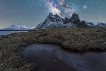 Picturesque scenery of rocky Krossanesfjall mountain range with uneven surface located near calm pond under blue sky with stars in Iceland - ADSF45055