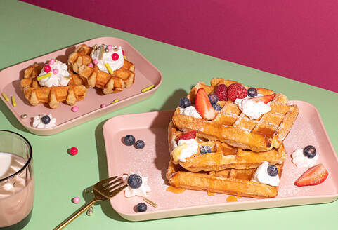 From above tasty sweet waffles topped with berries fruits sauce and cream served on pink tray on colorful table background near glass with hot milk beverage in light kitchen - ADSF45059