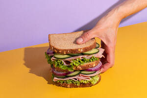 Cropped unrecognizable person holding delicious sandwich with tomatoes, cheese slices and fresh vegetables on colorful background - ADSF45063