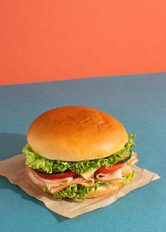 Delicious sandwich with ham, tomatoes, cucumber and cheese slices and fresh lettuce on blue and orange background - ADSF45065