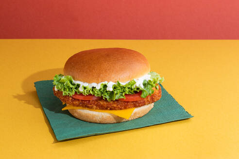 Delicious fish burger with tomatoes, cheese slices and fresh lettuce on yellow and red background - ADSF45067