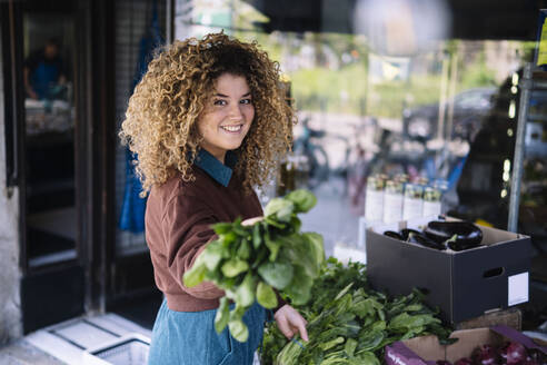 Smiling businesswoman holding leafy vegetables outside store - AMWF01463