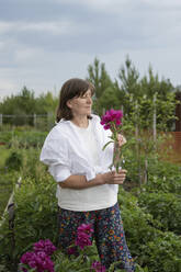 Ältere Frau riecht an einer Blume im Garten - LESF00338