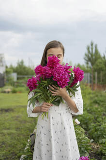 Girl smelling bunch of flowers in garden - LESF00340
