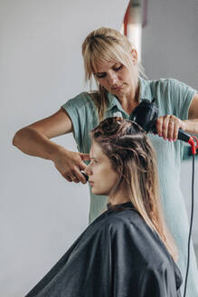 Friseurin föhnt das Haar eines Kunden im Friseursalon - VSNF01161