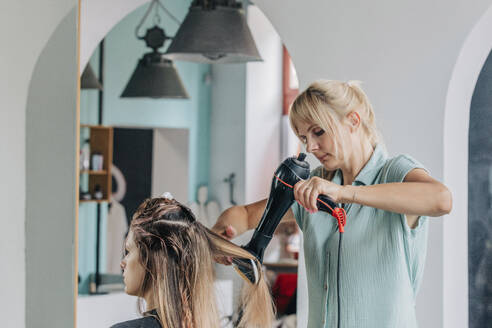 Friseurin föhnt das Haar eines jungen Kunden im Salon - VSNF01162