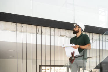 Architect examining and standing with document at construction site - MMPF00793