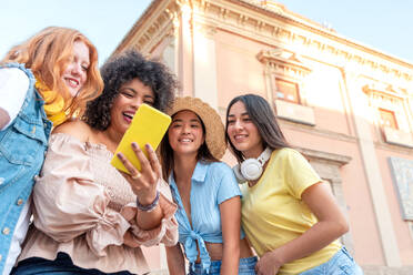 A diverse group of young women happily take a selfie while standing on a Valencia city street, with one holding the smartphone - ADSF45096