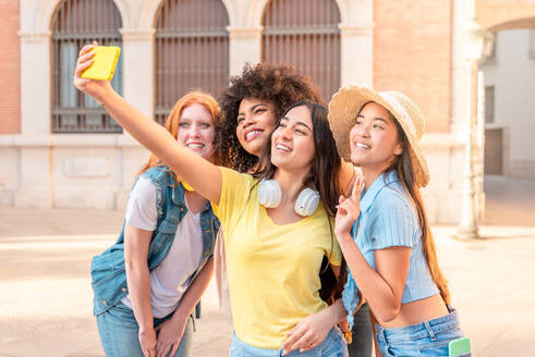 Eine Gruppe von Frauen posiert fröhlich für ein Selfie in einer Straße in Valencia, wobei eine Freundin das Smartphone hält - ADSF45115