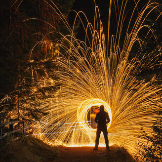 Back view of man standing in dark park with bright flames with long exposure effect - ADSF45169