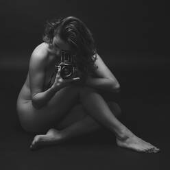 Seductive nude female with perfect body sitting with vintage photo camera on floor and looking at camera - ADSF45187