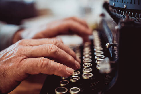 Shot of hands of anonymous elderly person typing on keyboard of vintage typewriter - ADSF45189