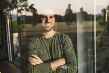 Smiling man with arms crossed seen through glass - UUF29399