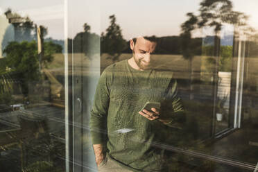 Man using smart phone seen through glass - UUF29401