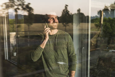 Happy man talking on smart phone seen through glass - UUF29402