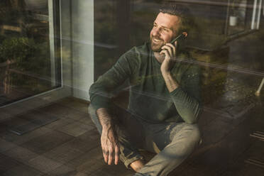 Happy man talking on smart phone sitting at home - UUF29405
