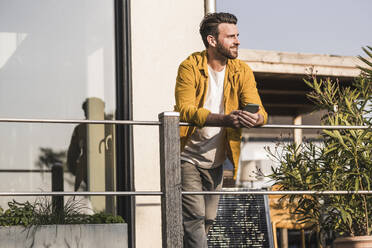 Lächelnder Mann mit Smartphone auf einer Terrasse stehend - UUF29420