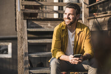 Happy man with mobile phone sitting on steps - UUF29426