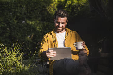 Smiling man using tablet PC and holding coffee cup - UUF29431