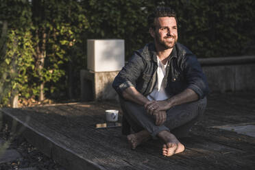 Nachdenklicher Mann sitzt auf Veranda - UUF29444