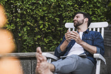 Nachdenklicher Mann sitzt mit Kaffeetasse auf einem Stuhl - UUF29456