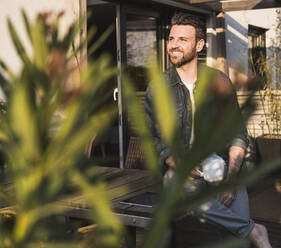 Smiling man sitting with coffee cup on terrace - UUF29470