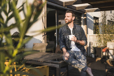 Nachdenklicher Mann sitzt mit Kaffeetasse auf der Terrasse - UUF29471