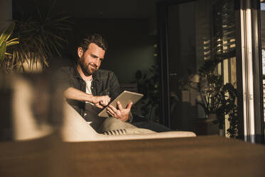 Lächelnder Mann mit Tablet-PC auf dem Sofa zu Hause - UUF29477