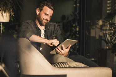 Happy man using tablet PC on sofa at home - UUF29478