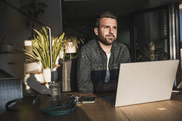 Freelancer with laptop sitting at desk - UUF29489