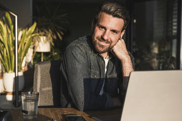 Smiling freelancer with laptop sitting at desk - UUF29493