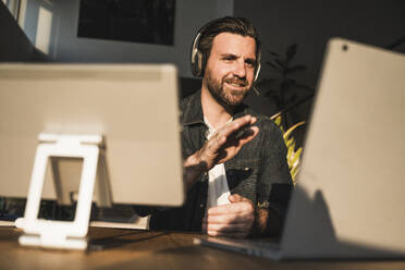 Happy freelancer wearing headset gesturing and talking on video call - UUF29499