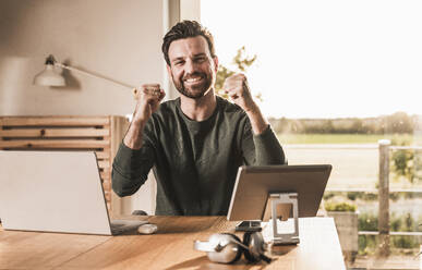 Successful happy freelancer cheering at desk - UUF29507