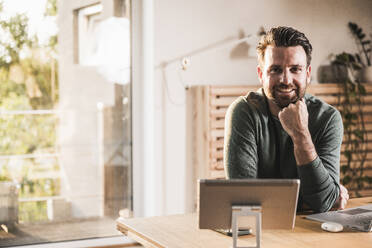 Smiling freelancer with hand on chin sitting at desk - UUF29511