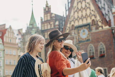 Eine fröhliche Familie hält einen Moment mit einem Smartphone-Selfie vor einem beeindruckenden Gebäude fest - VSNF01167