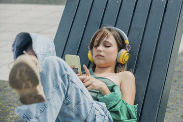Mädchen mit drahtlosen Kopfhörern und Smartphone auf einer Bank - VSNF01199