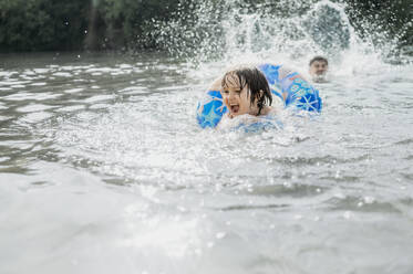 Glücklicher Junge schwimmt mit aufblasbarem Schwimmring im Wasser - ANAF01744