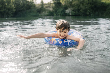 Happy boy with inflatable swim ring swimming in water - ANAF01747