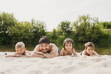 Vater liegt mit Kindern am Flussufer im Sand - ANAF01760