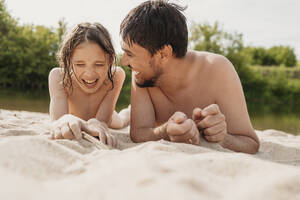 Fröhlicher Vater und Sohn liegen im Sand und genießen am Strand - ANAF01762