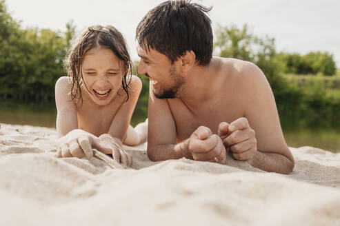 Cheerful father and son lying on sand and enjoying at beach - ANAF01762