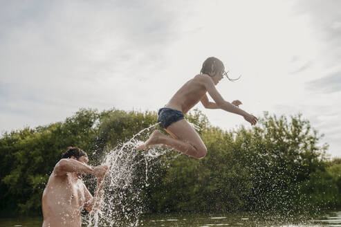 Vater mit Sohn springt an einem sonnigen Tag ins Wasser - ANAF01768