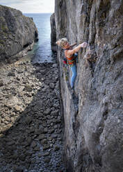 Adventurous woman climbing rocky mountain in Pembrokeshire - ALRF02097