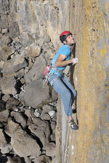 Entschlossener Mann klettert an einem sonnigen Tag auf einen felsigen Berg - ALRF02099