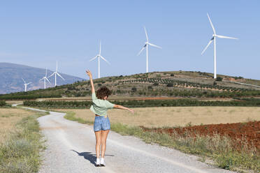 Frau steht mit erhobenen Armen vor Windkraftanlagen an einem sonnigen Tag - LMCF00368