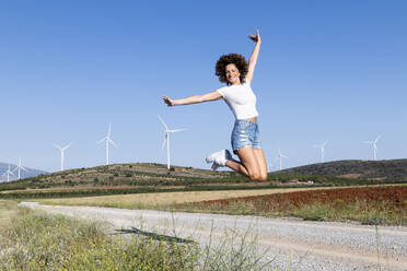 Fröhliche Frau springt vor Windkraftanlagen - LMCF00380
