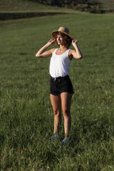 Smiling woman wearing hat standing on grass - LMCF00395