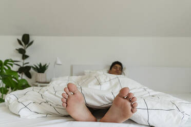 Young man with barefoot resting on bed at home - OSF01864