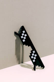 Trendy black pixel sunglasses placed on white table and leaned on gray wall in studio - ADSF45206