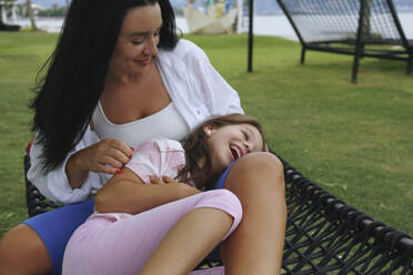 Smiling mother spending time with daughter on hammock - SYEF00485